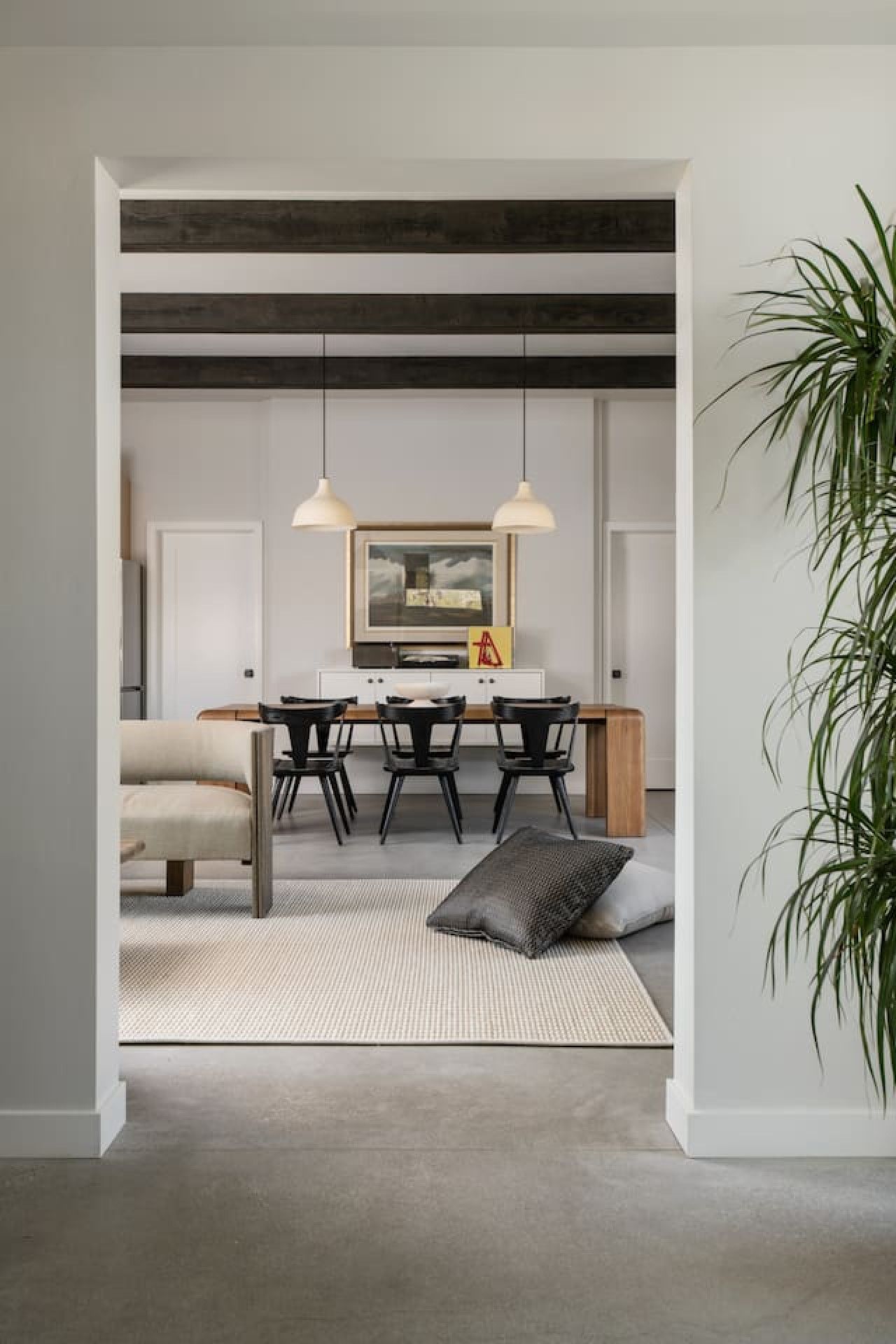 Uma área de jantar moderna com mesa de madeira, cadeiras pretas e iluminação pendente.