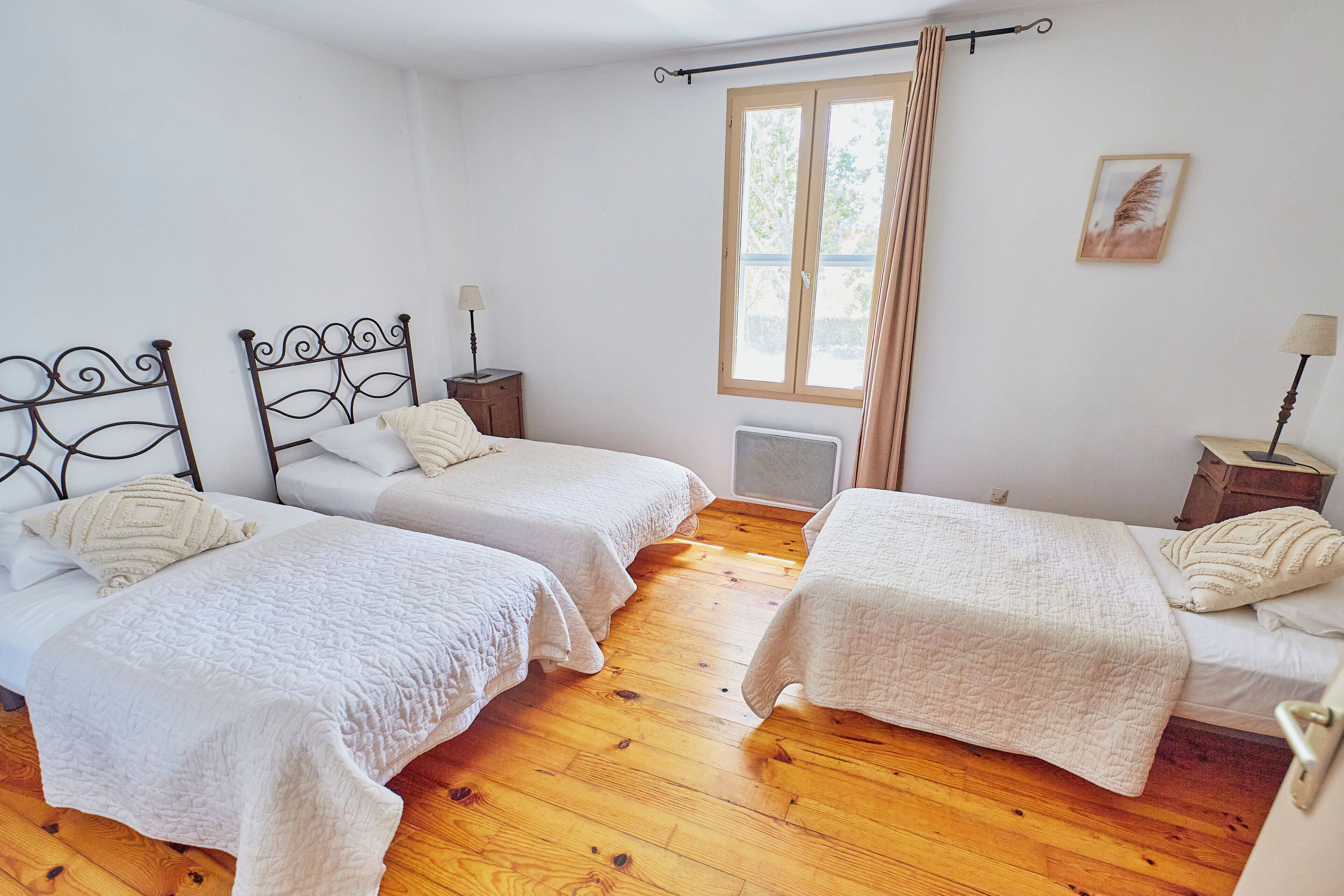A room with two beds, wooden flooring, a window with curtains, and a radiator.