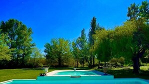 A rectangular swimming pool with a clear blue water, surrounded by a well-maintained lawn and trees.