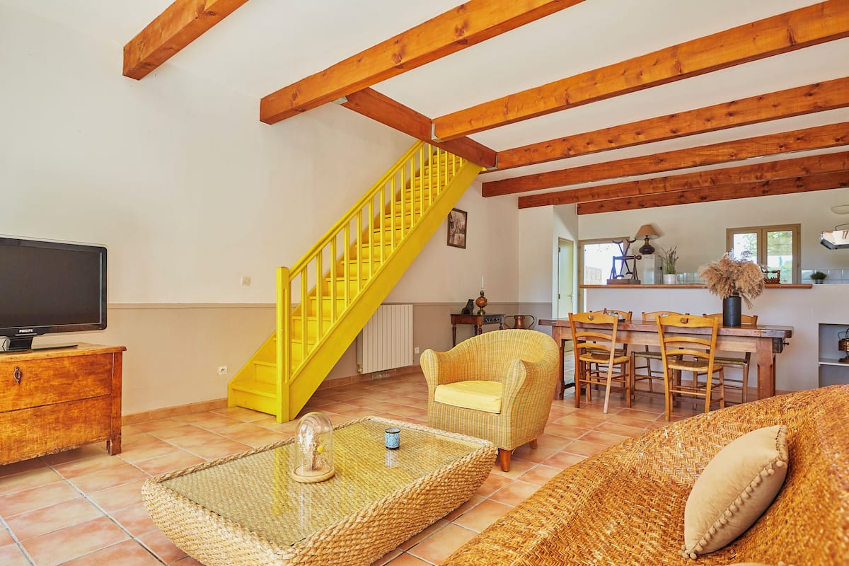 A living room with a yellow staircase, a television, wicker furniture, and a dining area.