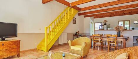 A living room with a yellow staircase, a television, wicker furniture, and a dining area.