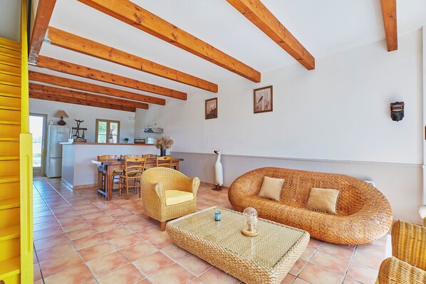A spacious living area with a dining table, wicker furniture, and a kitchen in the background.