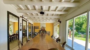 A long wooden table with chairs in a room with a high ceiling and large windows.