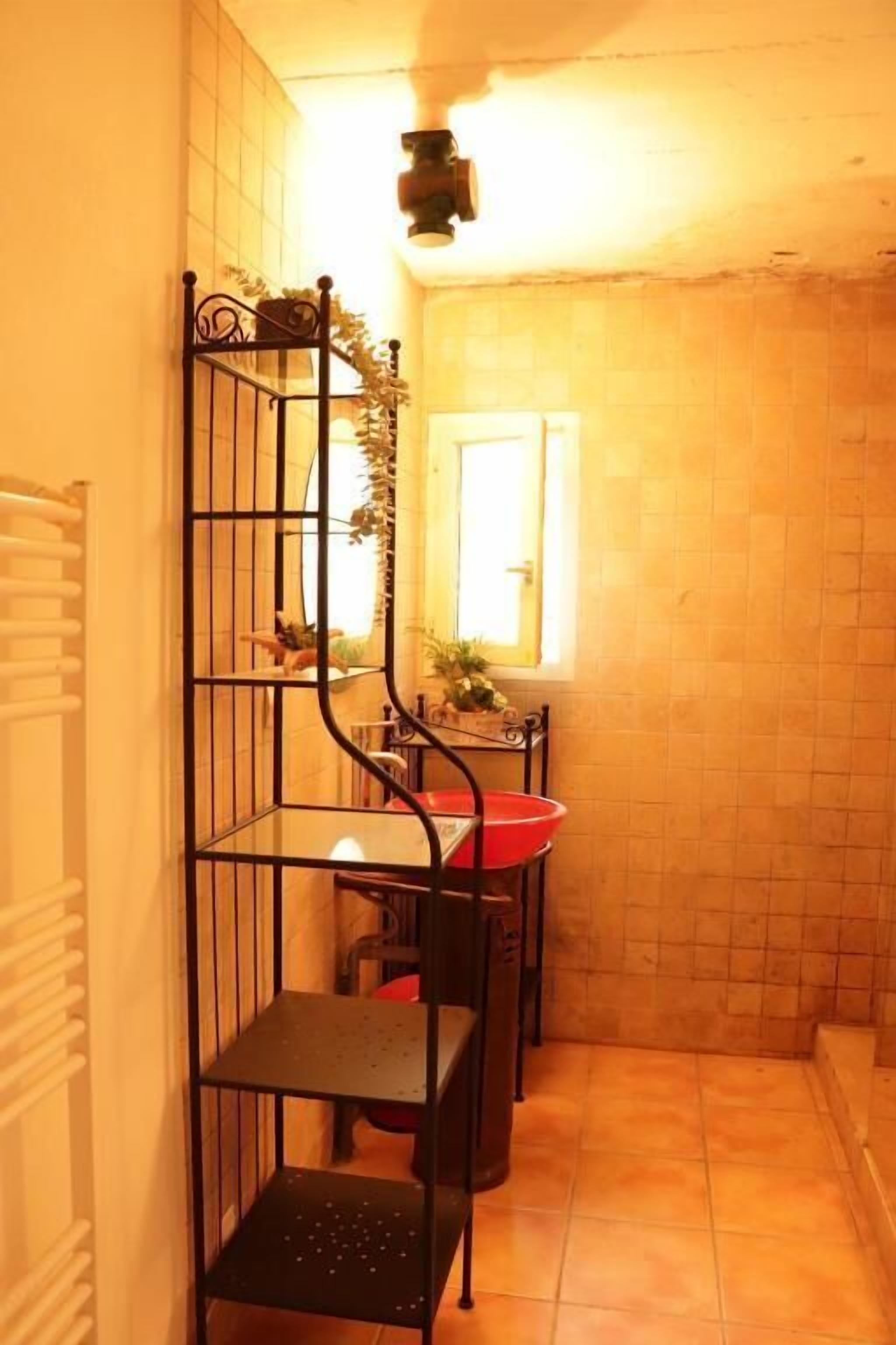 A narrow hallway with a black metal shelf unit against the wall, a red basin, and a window with a view of the outside.