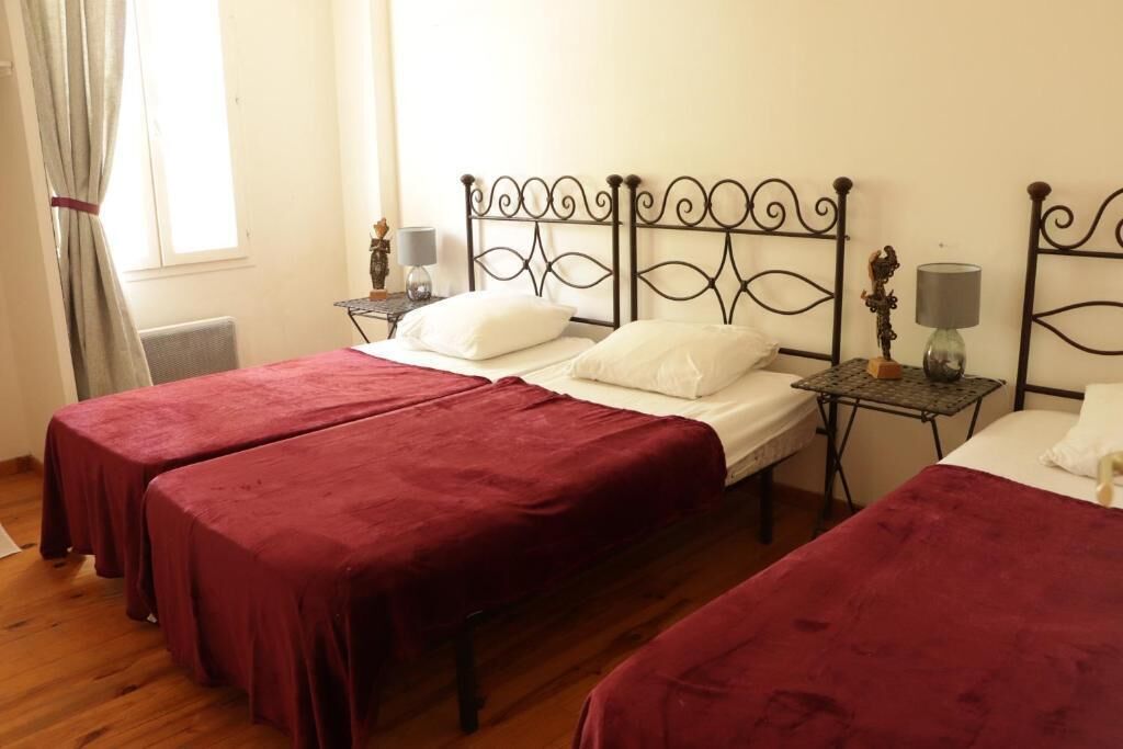 A room with two single beds, each with a red bedspread, a small bedside table with a lamp, and a decorative item.