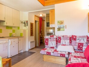 A compact living space with a kitchenette, a sofa with a quilted cover, and a dining table.