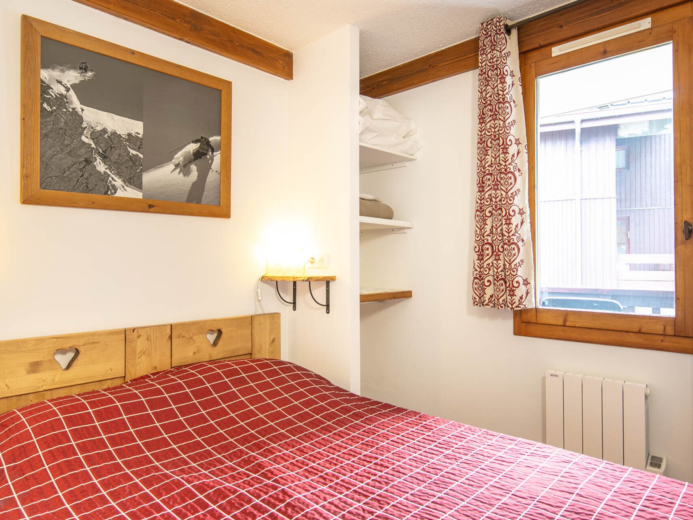 A bedroom with a bed, a wall-mounted shelf, a window with curtains, and a picture on the wall.