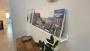 A hallway with a wooden bench, a potted plant, and a wall-mounted shelf displaying magazines and a city guide.
