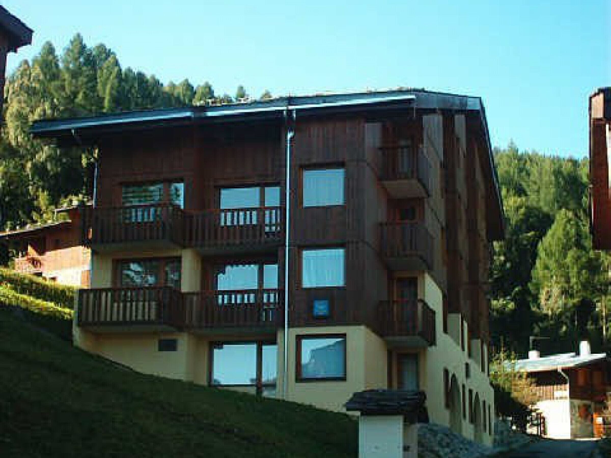 A multi-story building with balconies, large windows, and a sloped roof.