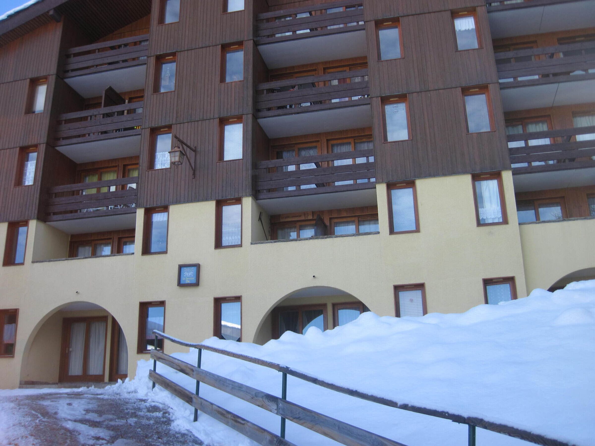 Un immeuble à plusieurs étages doté de balcons, un sol recouvert de neige et une clôture en bois.