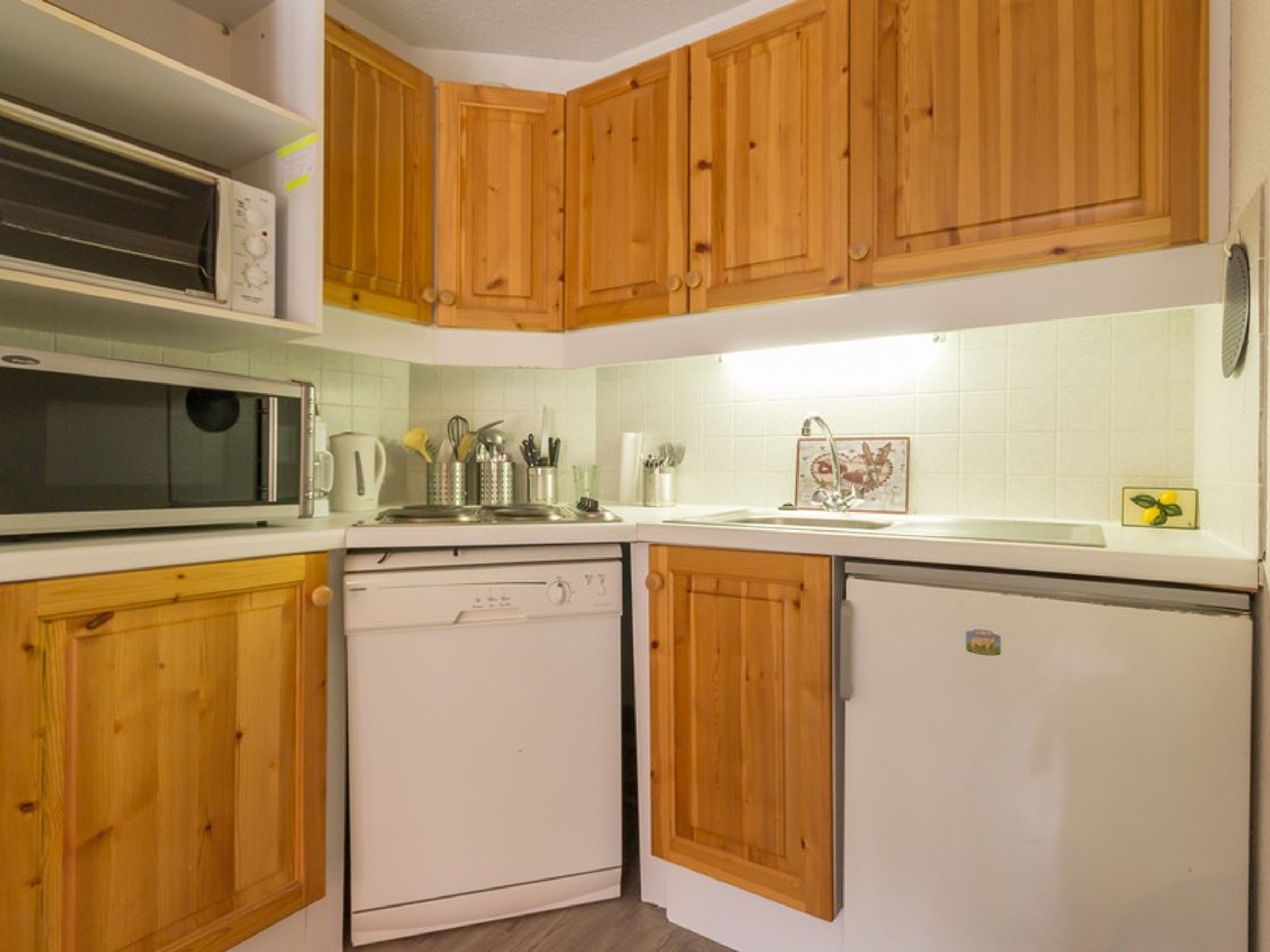 Eine kompakte Küche mit Holzschränken, einer Mikrowelle, einem Geschirrspüler und einem Kühlschrank.