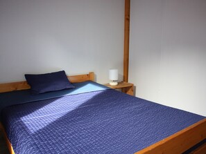 Una cama con un edredón azul, un cabecero de madera y una lámpara blanca sobre una mesita de noche de madera.