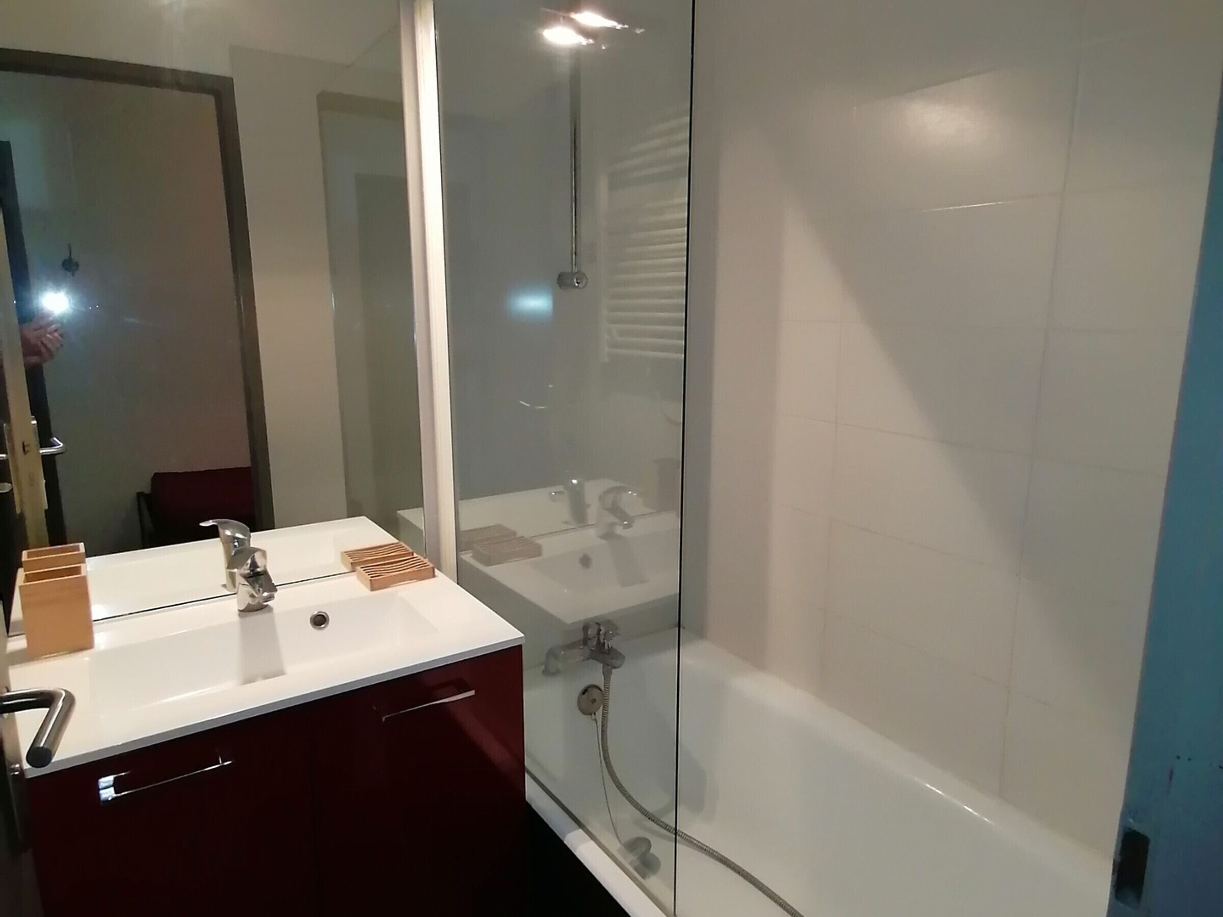 A modern bathroom with a glass-enclosed shower, a white sink with a mirror, and a red vanity.