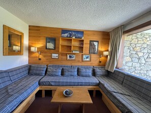 A cozy room with a wooden wall, a sofa, a table, and a stone wall outside. - 5 person apartment at the foot of the slopes with terrace, pets allowed (Belle Plagne)