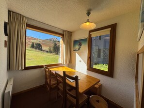 A room with a wooden dining table, four chairs, a ceiling fan, and a window with curtains. - 5 person apartment at the foot of the slopes with terrace, pets allowed (Belle Plagne)