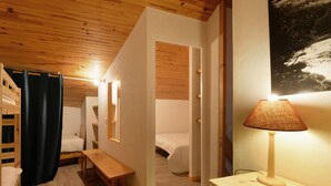 A cozy room with a wooden ceiling, a bench, a bedside table with a lamp, and a bed with a headboard.