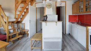 A compact kitchen with wooden staircase, white cabinets, and a red backsplash.