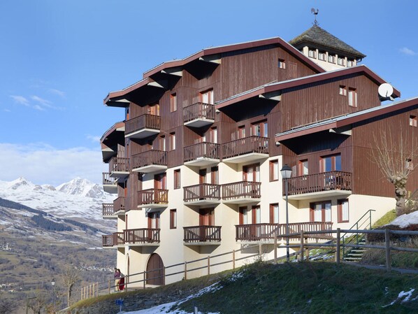 Een hotel met meerdere verdiepingen, balkons, een stenen trap en uitzicht op besneeuwde bergen.