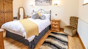 A bedroom with a bed, wooden nightstands, a bedside table, a chair, a radiator, a mirror, and a painting on the wall.