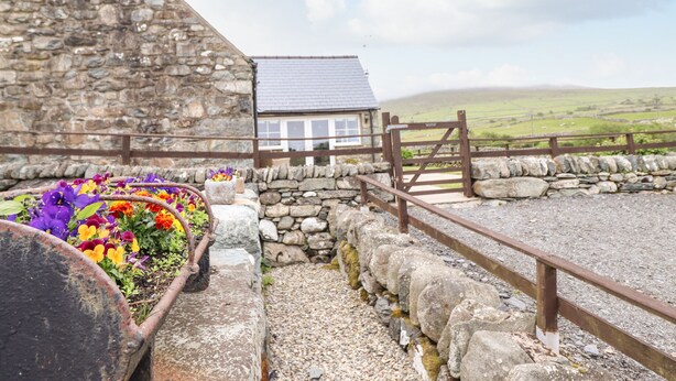 A stone building with a small house, a flower bed with colorful flowers, and a stone wall with a wooden fence.