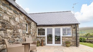 A stone building with a tiled roof, a glass door entrance, wicker furniture, and a stone wall.