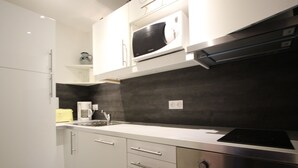 Una cocina moderna con armarios blancos, microondas integrado, estufa de acero inoxidable y cafetera.