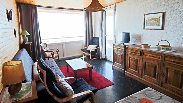 Una sala de estar acogedora con techo de madera, un sofá, un sillón, una mesita y un televisor sobre un mueble de madera.