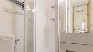 A bathroom with a glass-enclosed shower, a toilet, and a sink with a mirror.