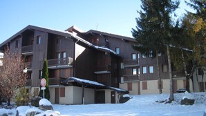 Ein mehrstöckiges Gebäude mit Balkonen, einem überdachten Eingang und einem mit Schnee bedeckten Gelände.