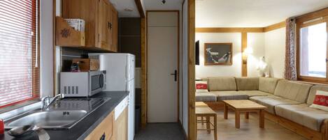 A compact kitchen with modern appliances, a dining area with a sofa and table, and a view of the outdoors through a window.