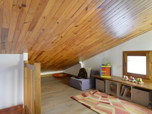 A cozy attic room with a sloped wooden ceiling, a small sofa, a colorful toy train set, and a window.