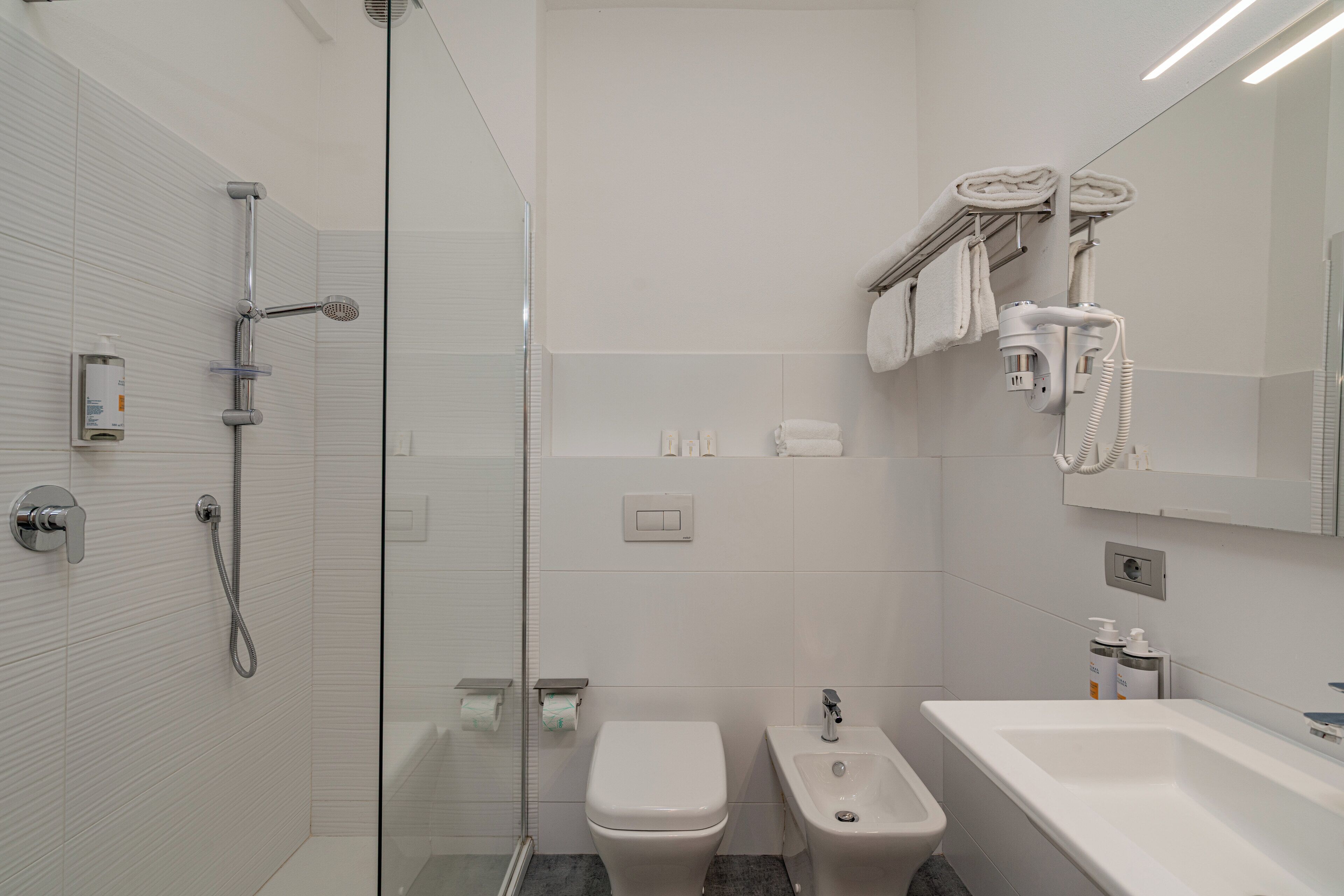 Ein modernes Badezimmer mit einer Glastrennwand-Dusche, einer Toilette, einem Bidet und einem Waschbecken.