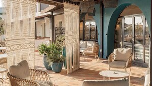 Área de pátio externo com móveis de vime, cortinas de macramé e plantas em vasos.
