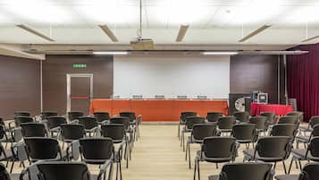Un salón de conferencias con filas de sillas mirando hacia un escenario con una pantalla de proyección.