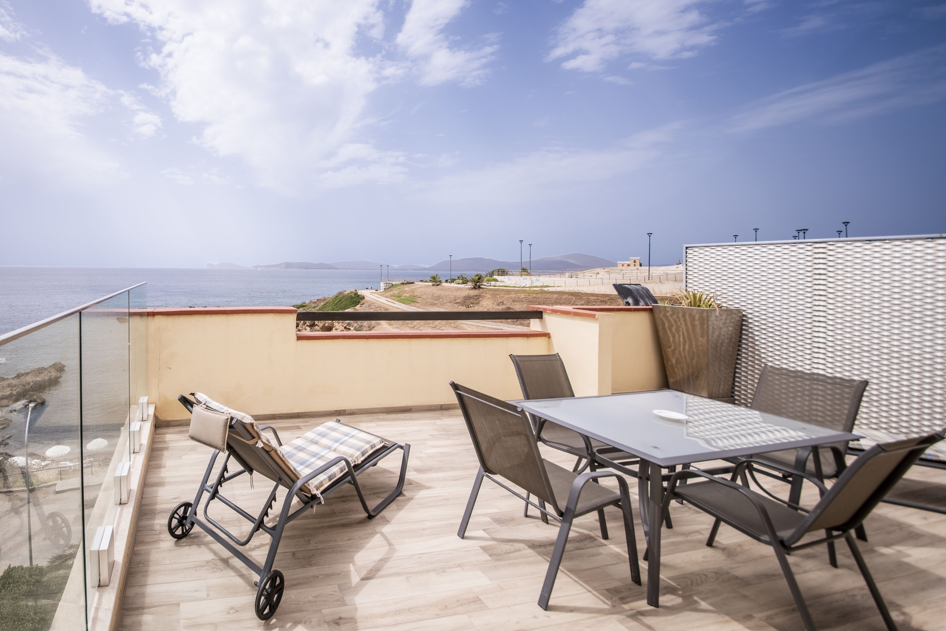 A balcony with a table and chairs, overlooking a beach and the sea.