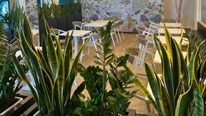 Uma sala de jantar moderna com luminárias de palha no teto, mesas brancas e plantas verdes.