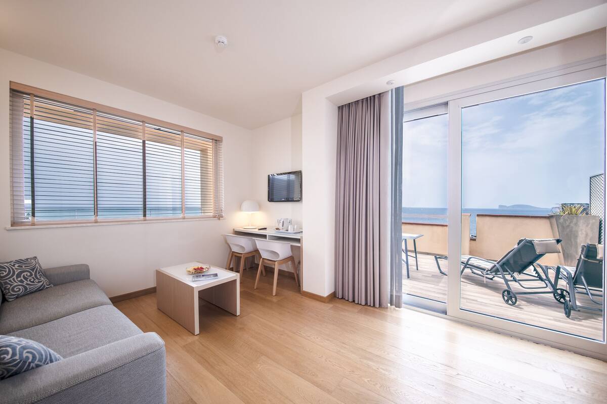 Une chambre d’hôtel moderne équipée d’un canapé, d’un bureau avec des chaises, d’une petite table, d’une télévision et d’un balcon avec vue.