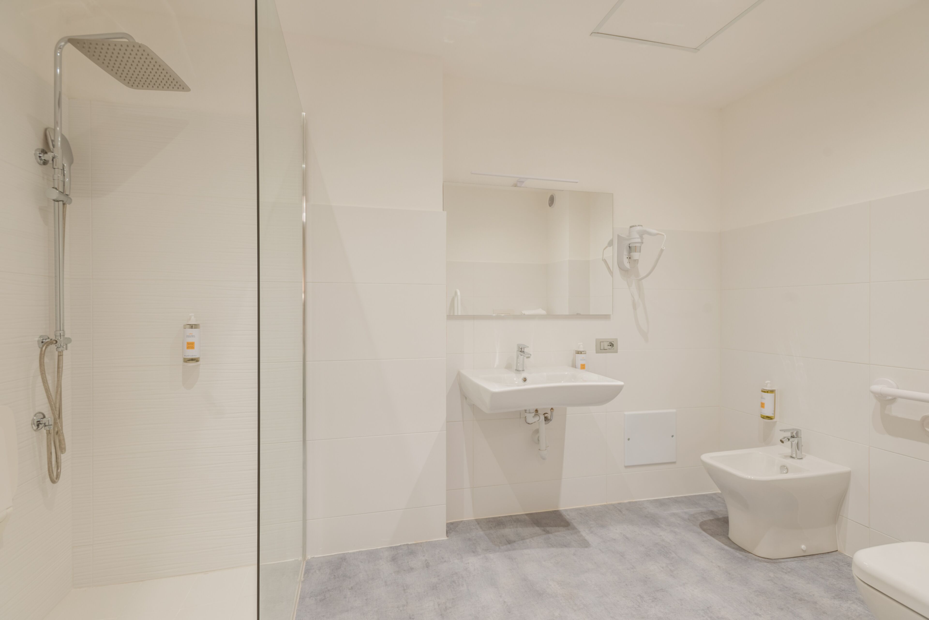 A modern bathroom with a glass shower enclosure, a sink, a bidet, and a toilet.