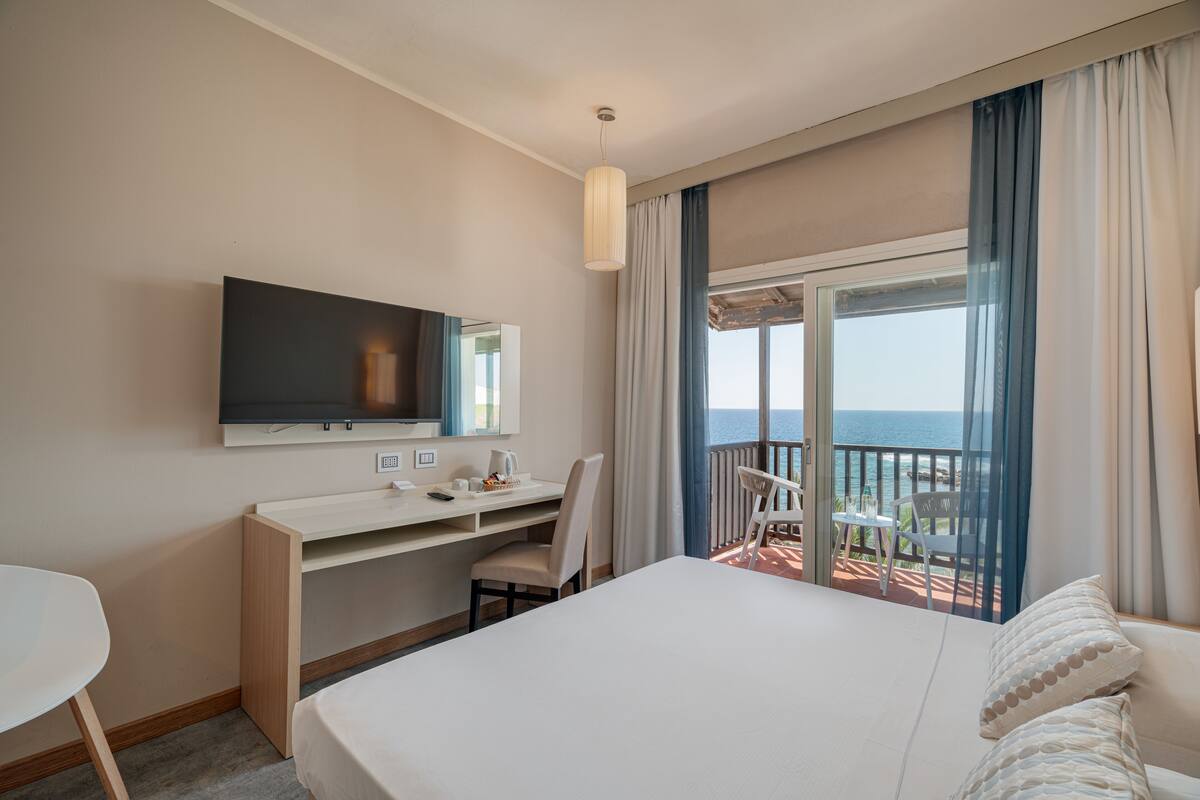 Une chambre d’hôtel comprenant un lit, un bureau, une chaise, une télévision et un balcon avec vue sur la mer.