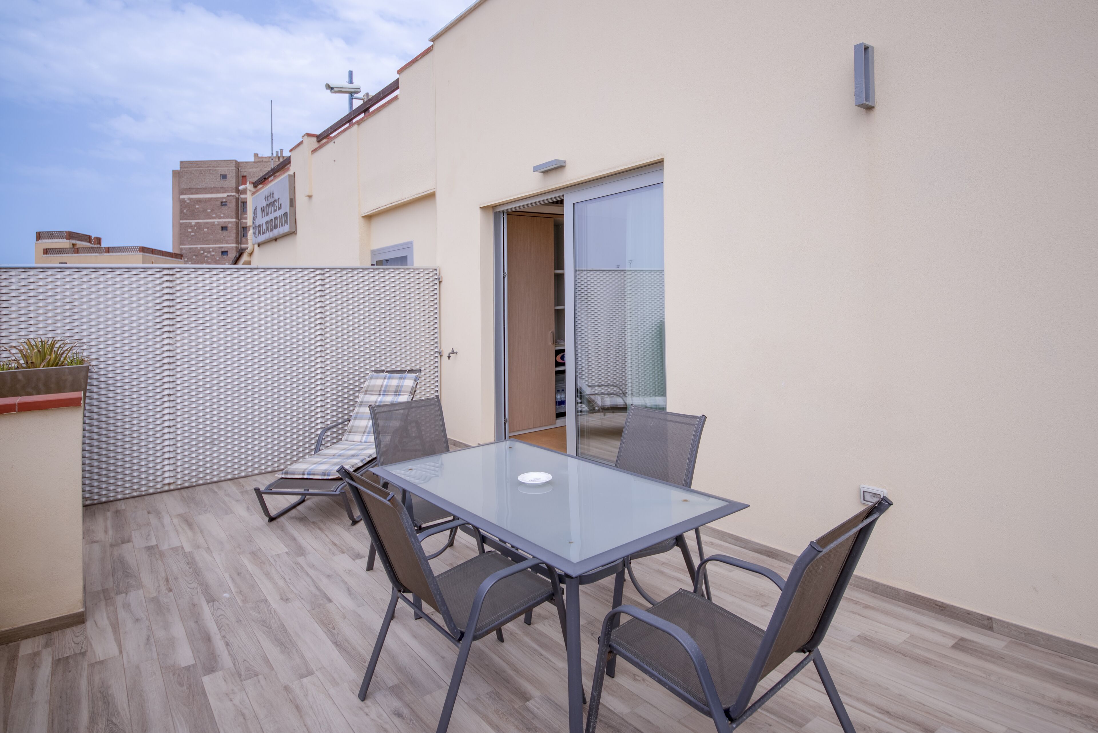 Mesa de vidrio con cuatro sillas en un patio al aire libre con suelo de baldosas.