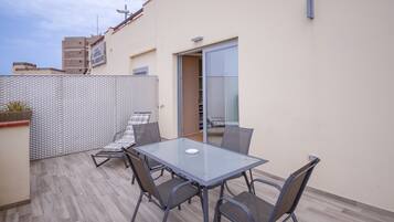 Mesa de vidrio con cuatro sillas en un patio al aire libre con suelo de baldosas.