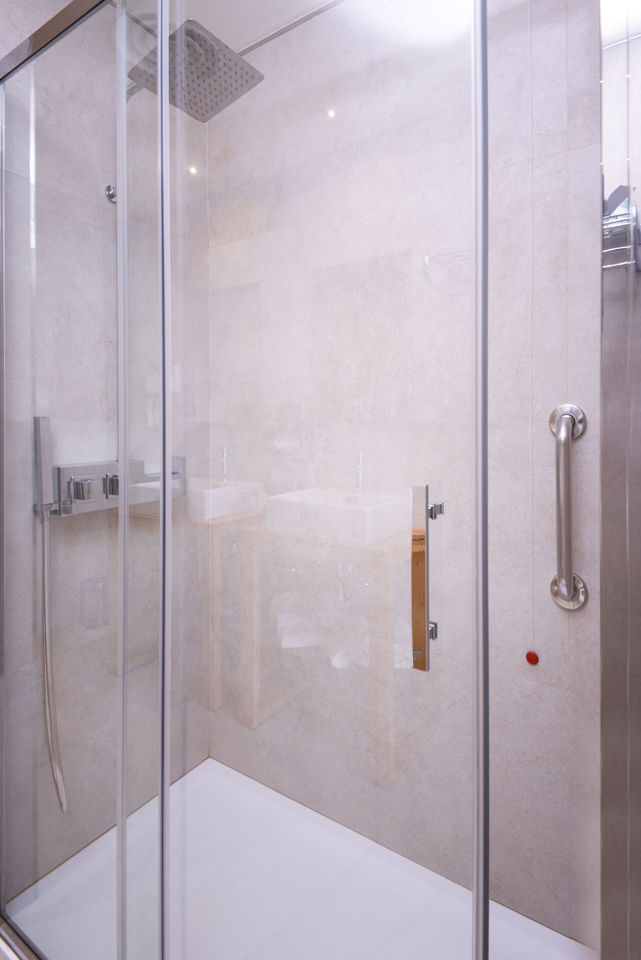 A modern shower enclosure with a glass door, a handheld showerhead, and a wall-mounted control panel.