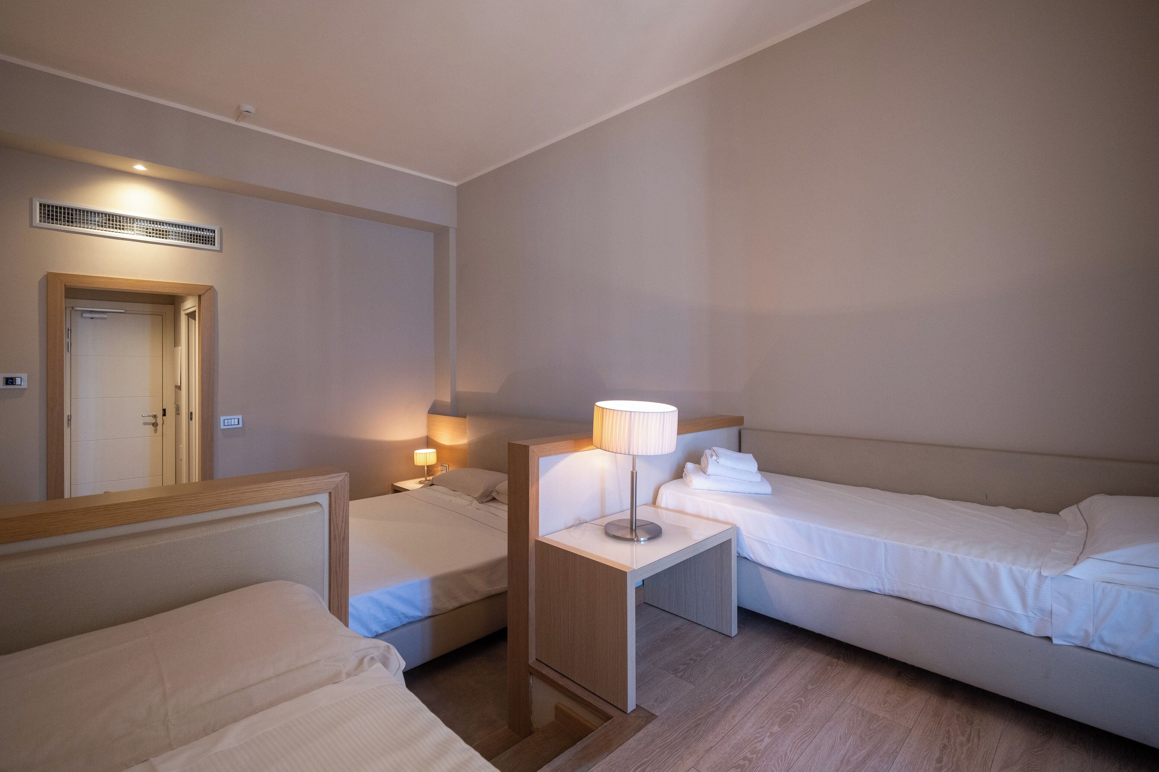 Et hotelværelse med to senge, et natbord med lampe og et lille bord.