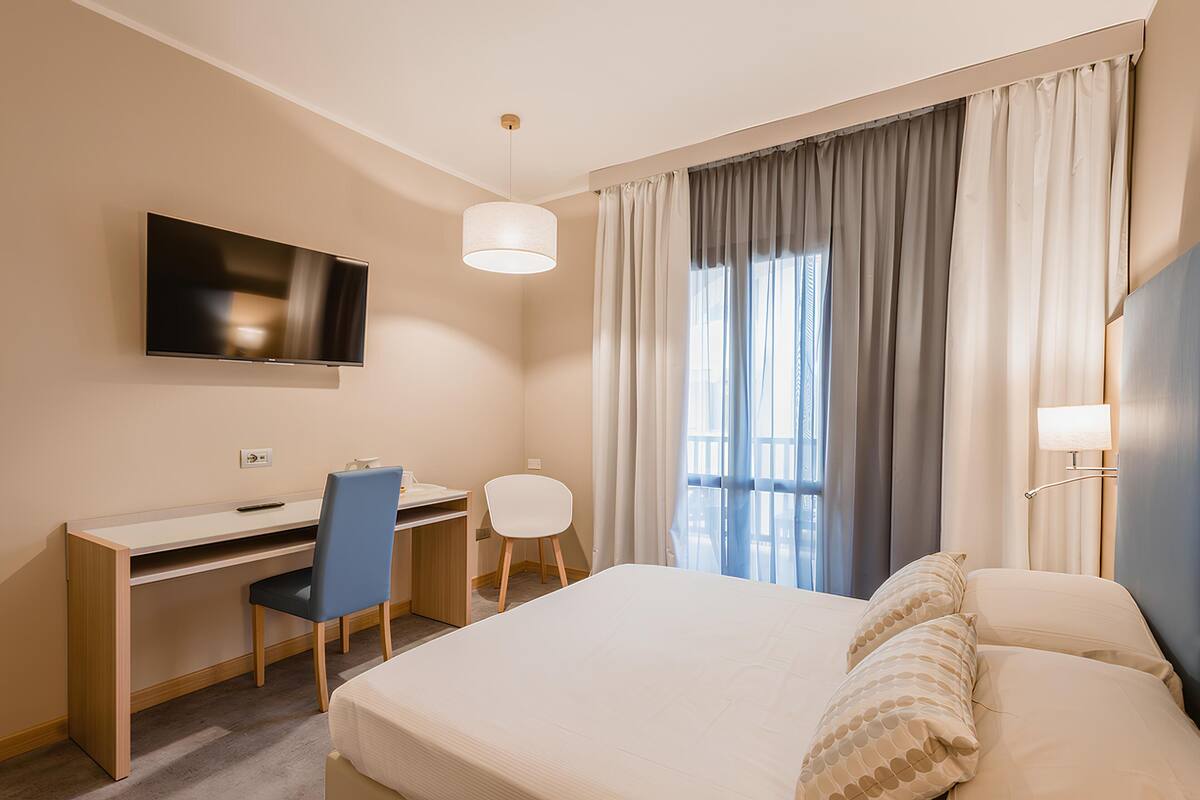 Une chambre d’hôtel équipée d’un lit, d’un bureau, d’une chaise, d’une télévision et d’une fenêtre avec des rideaux.