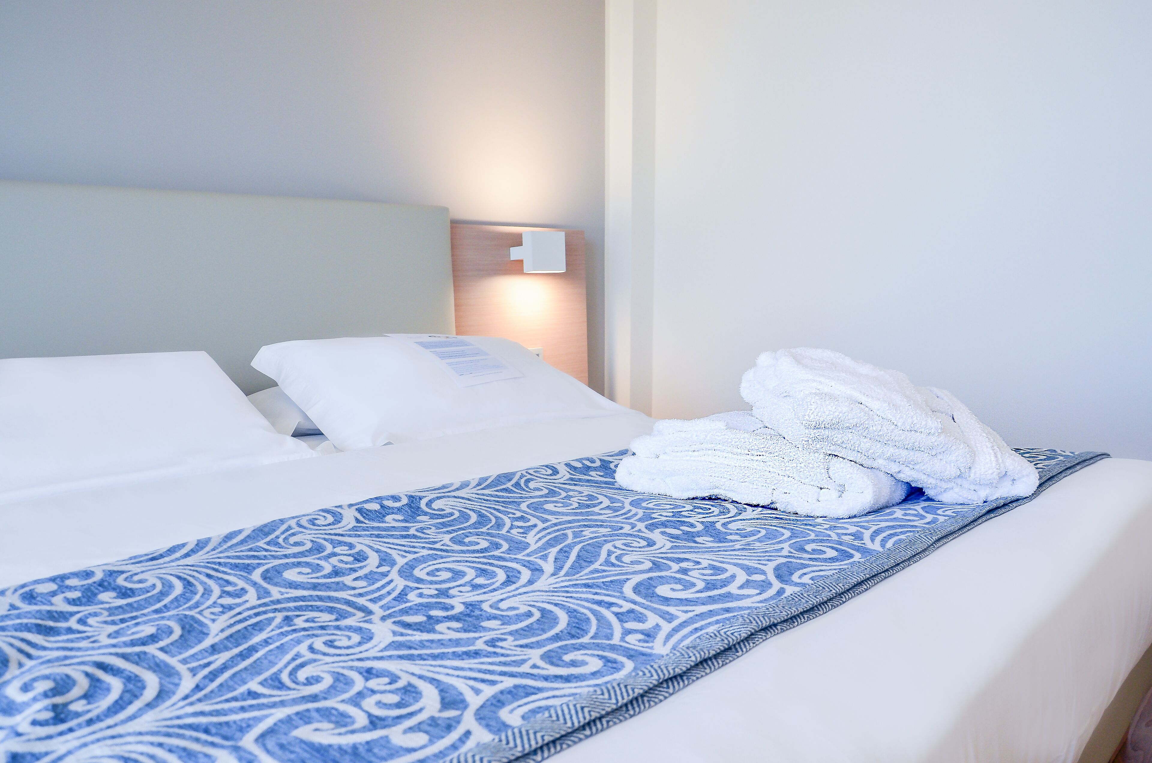 Una cama bien hecha con una colcha azul estampada y almohadas blancas.