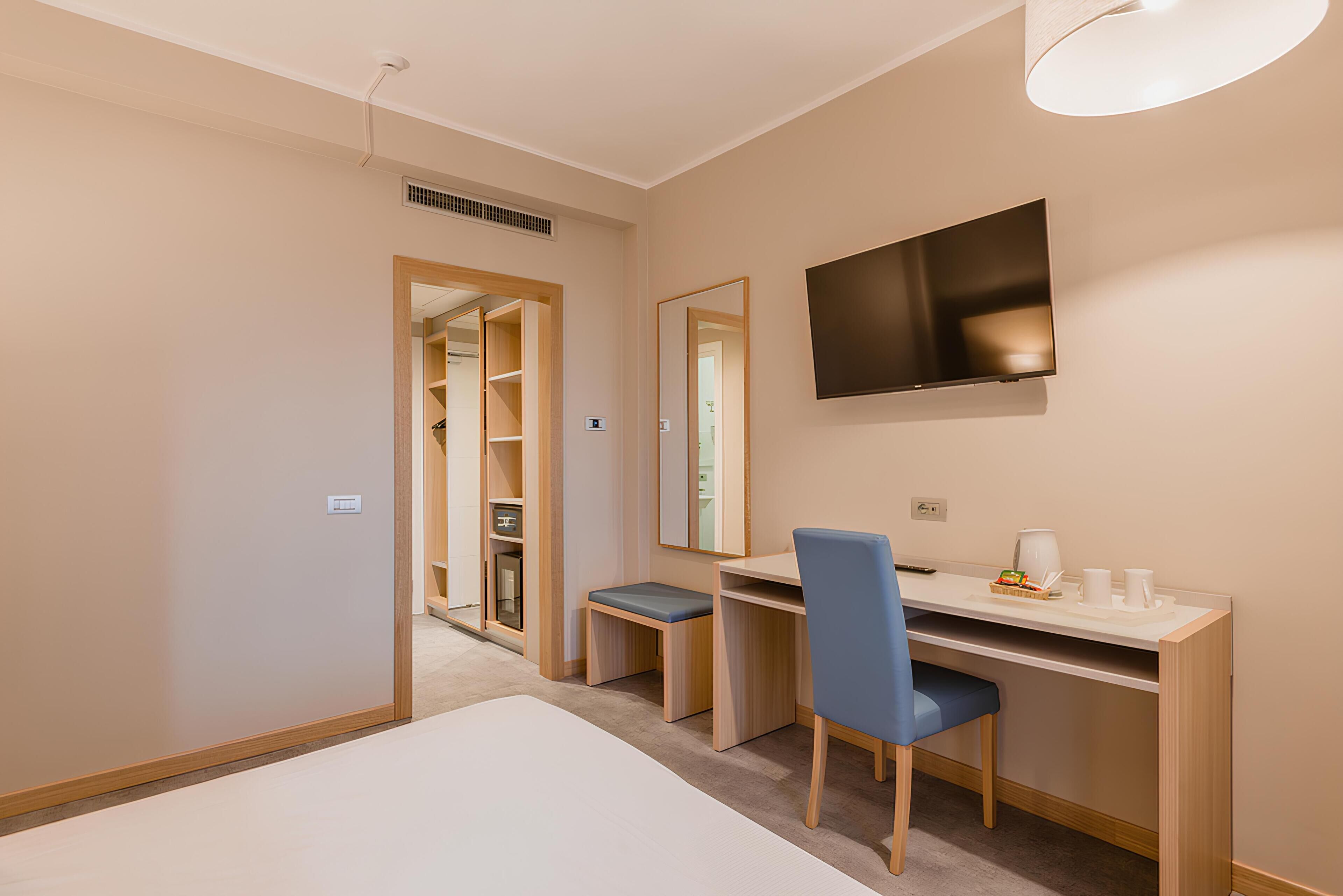 A hotel room with a bed, a desk with a chair, a television, and a mirror.