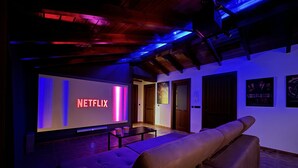 Una camera accogliente con un grande schermo che mostra 'NETFLIX', un divano confortevole e un soffitto in legno.