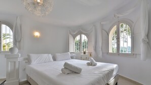 A large, neatly made bed in a bright, white room with arched windows and a chandelier. - Holiday Villa Moraira with private heated pool in walking distance to beaches (Moraira)