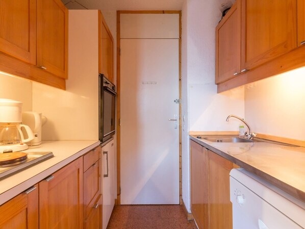 A compact kitchen with wooden cabinets, a coffee maker, a microwave, and a sink.