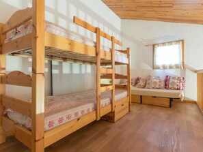 A bunk bed with a lower bunk and a ladder, a wooden bench with cushions, and a window with curtains.